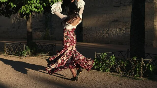 Gypsy woman in traditional dress dancing flamenco in a park at sunset on a sunny day