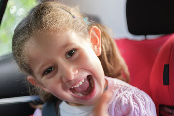 Transport, safety, childhood road trip and people concept - happy little girl sitting in car. Happy Little caucasian girl child showing front teeth with big smile. selective Focus teeth.