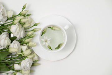 Floral tea. White cup with fragrant herbal tea and Eustoma Lisianthus flowers near. Tea time. Relaxing with herbal tea, white background, top view, vertical