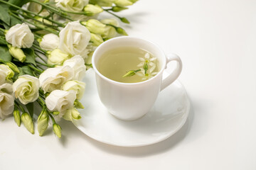 Obraz na płótnie Canvas Healthy herbal tea in a white cup with Lisianthus flowers for relaxation and wellness. Floral Infusion, tea drinking ritual for a healthy lifestyle