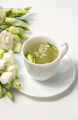 Floral tea. White cup with fragrant herbal tea and Eustoma Lisianthus flowers near. Tea time. Relaxing with herbal tea, white background, top view, vertical