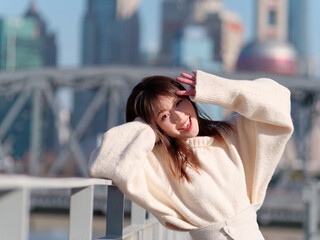 Beautiful young woman with black long hair in white skirt smiling  with Shanghai garden bridge background (Waibaidu bridge) in sunny day. Emotions, people, beauty, travel and lifestyle concept.