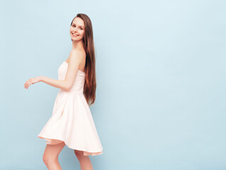 Naklejka premium Portrait of young winsome woman in romantic attire pretty smiling on blue background. Slim female in pure pink dress posing in studio. Cheerful model. Isolated. Long hair