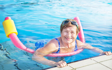 Active senior woman (over age of 50) in sport goggles, swimsuit doing aqua fitness with swim...