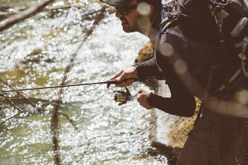 Pescatore in azione durante una battuta di pesca nelle acque di un torrente montano in Trentino Alto Adige, Italia - obrazy, fototapety, plakaty