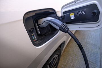 Close up of a white electric car being charged by a charging station
