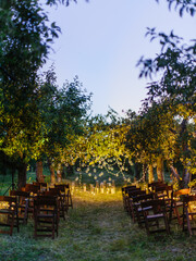 Wedding ceremony in the garden. Rows of chairs on the lawn, green trees, an altar decorated with candles and garlands.