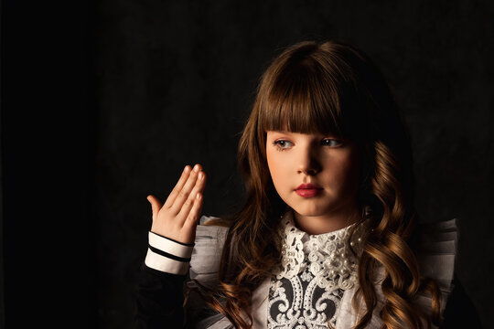 Portrait of cover girl in doll image gestured hand isolated in shadow, frozen pose looking away. Pretty kid 9-10 year old with curly hair at black background. Theatrical show concept. Copy text space