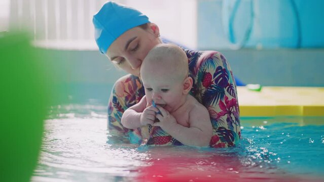 Portrait Of Female Swimming Coach With Little Baby On Hands In Water Of Pool