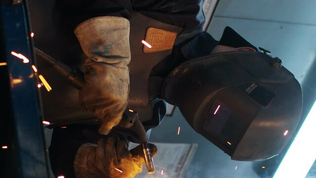 Vertical shoot. Asian welder solder the iron. Man at workshop surrounded by tools. Worker dressed in special apron and safety gloves. Male lifts up protective masc. Diversity of professions.