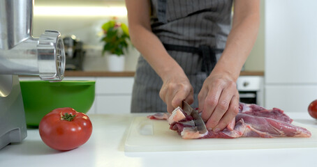 Close-up view of woman cutting up fresh meat with a knife on a kitchen board.