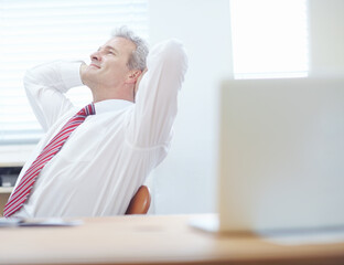 Thinking about success. Relaxed businessman leaning back in an office chair with his hands behind...