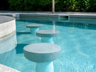 Empty round terrazzo bar stools seat in clean and clear water swimming pool preparing for the...