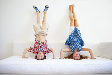 Ta da. a playful young brother and sister doing handstands together on the sofa.