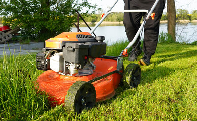 Lawn mowing. Person mowing the grass with orange lawnmower. Mowing in the summer on sunny day.