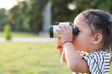 Happy cute little girl 3 years old stands in nature , holds binoculars.