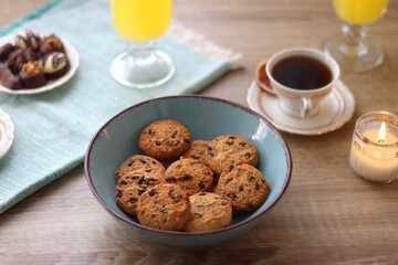 Plate of chocolate pralines, bowl of cookies, cups of tea, glasses of juice and lit candles on the table. Selective focus.