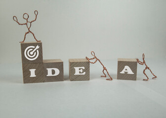 Wspólne dążenie do osiągnięcia celu. Napis IDEA na drewnianych klockach układanych przez postaci z drutu. - obrazy, fototapety, plakaty