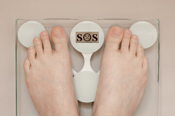female legs on the scales, the word SOS on the display, weighing on the scales, the concept of overweight, abdominal obesity