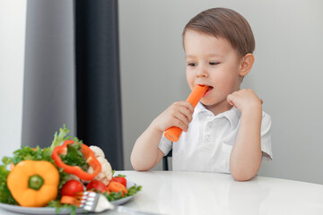 boy with appetite eats carrots and fresh vegetables at the table at home, the concept of a healthy diet for children