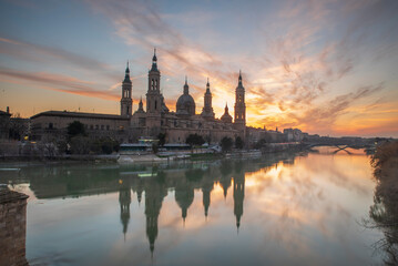 Obraz premium del Pilar basilica, one of the important architectural symbols of zaragoza, and the Ebro river and its reflection with sunset colors and clouds