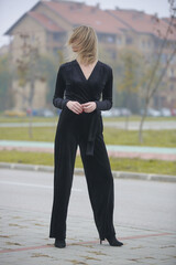 Outdoor portrait of woman in black velvet jumpsuit in the city, fall fashion collection