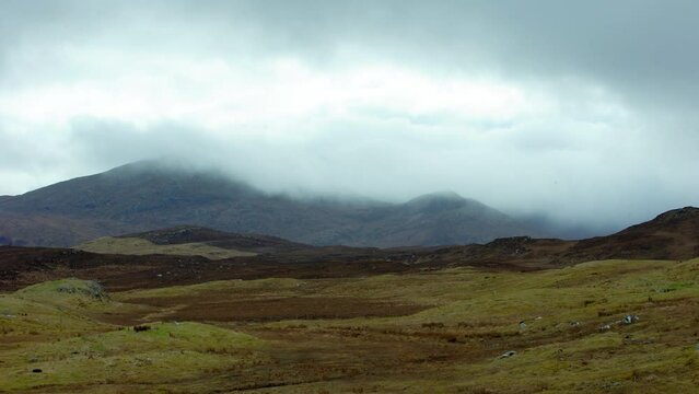 Static shot of a misty mountain range behind a peatland moor covered in heather. Filmed near Stornoway on the Isle of Lewis, part of the Outer Hebrides of Scotland.