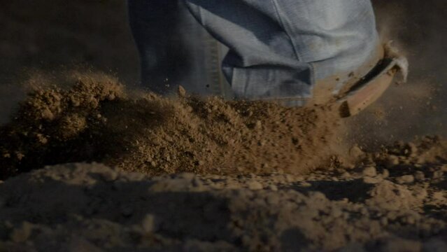 Cowboy boots kicking up dirt while backing up from a bull during a rodeo event.