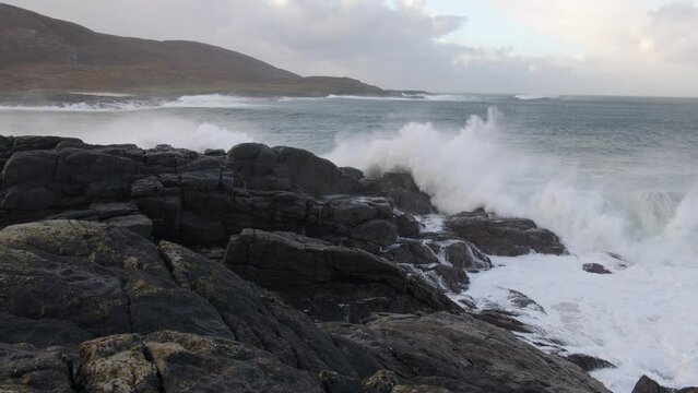 Slow motion shot of large, white wave combers breaking over the rocks during a storm in the bay by Tangasdale beach, near Castlebay on the Isle of Barra. Filmed on the Outer Hebrides of Scotland.