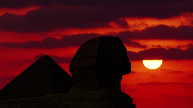 Majestic Sphinx located in the middle of the amazing and ancient pyramids in Egypt, with clouds and sun at dawn in time lapse.