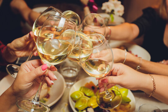 Close Up Shot Of Group Of People Clinking Glasses With Wine Or Champagne In Front Of Bokeh Background. Older People Hands.