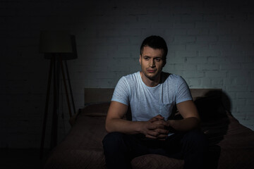 depressed man in white t-shirt sitting on bed while suffering from ptsd.