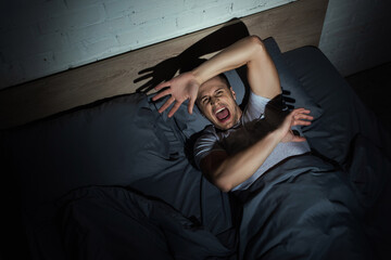 top view of stressed man screaming while having nightmares and panic attacks at night.