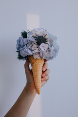 Anonymous woman holding ice-cream cone with hydrangea and other fresh flowers  - 599551583