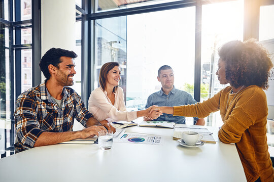 Combining their expertise to deliver excellence. two designers shaking hands during a meeting in an office.