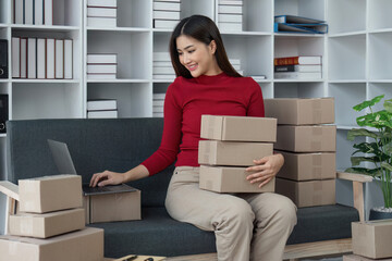 Female seller write the customer's address on the parcel box to prepare for delivery and using laptop checking day's sales on the online store, Concept of parcel delivery and selling online