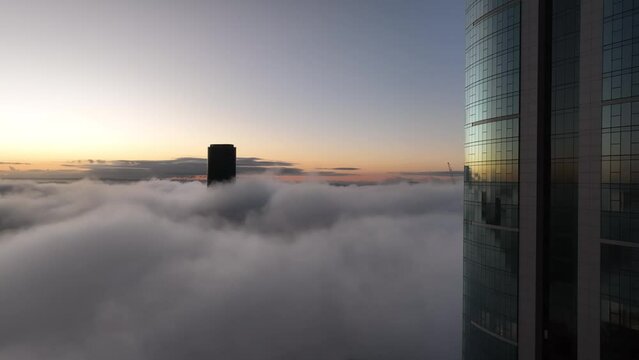 Aerial shot above a cloudy foggy Brisbane City, with only the tops of sky scrapers being visible. Sunrise. Flying nearby to a tall skyscraper. Camera facing Brisbane Skytower 222 Margaret St