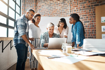 Growing businesses thrive on teamwork. a group of colleagues using a laptop together in a modern office.