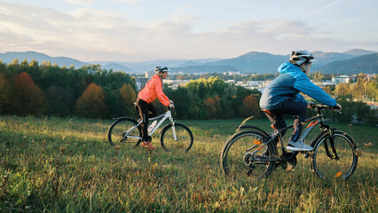 Obraz premium Mother and son ride bike outdoors. Happy cute boy in helmet to riding a bike in park on green meadow at sunset time. Family weekend. mothers Day