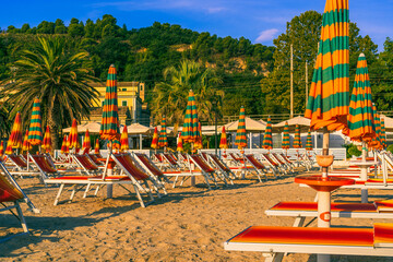 happy beautiful italian beach scene, row of lounge chairs on a sandy beach, yellow buildings with red roofs,railroad poles, mediterranean beach background, bright green dark orange, beach setting - obrazy, fototapety, plakaty