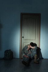 Soldier with mental disorder sitting near backpack and door at home at night.