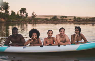 Diverse group of friends having fun while swimming at a lake in summer with a floating kayak boat. Happy, young and multiracial people on vacation enjoying nature and water on a canoe at sunset.