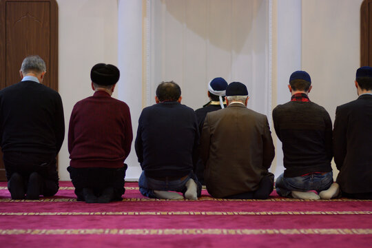 Group of Muslim men and mullah kneeling and praying in a mosque