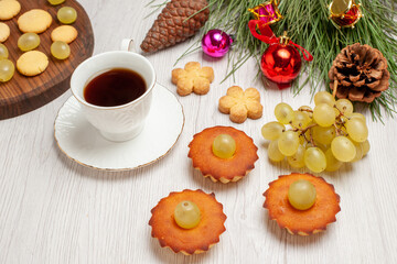front view delicious little cakes with grapes and cup of tea on white desk pie cake tea biscuit cookie