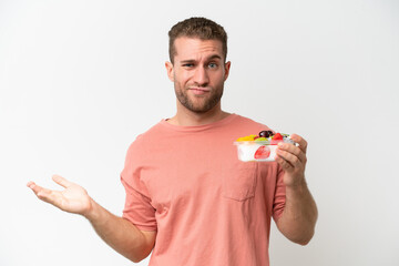 Young caucasian man holding a bowl of fruit isolated on white background making doubts gesture while lifting the shoulders