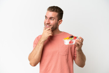 Young caucasian man holding a bowl of fruit isolated on white background thinking an idea and looking side