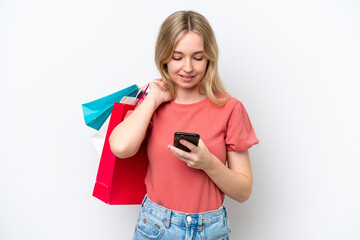 Young English woman isolated on white background holding shopping bags and writing a message with her cell phone to a friend