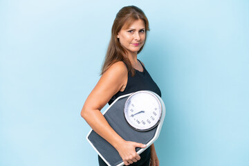 Middle-aged caucasian woman isolated on blue background with weighing machine