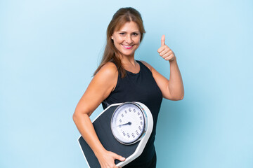Middle-aged caucasian woman isolated on blue background holding weighing machine with thumb up