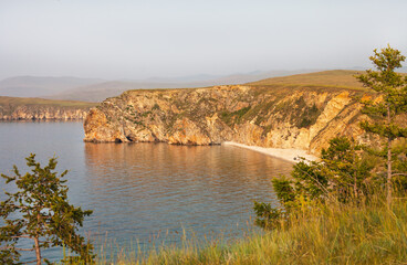 Picturesque landscape of Baikal Lake at sunset. Top view of the sandy beach of the cozy bay of Olkhon Island on a foggy hot evening. Summer travel, hiking and outdoor recreation